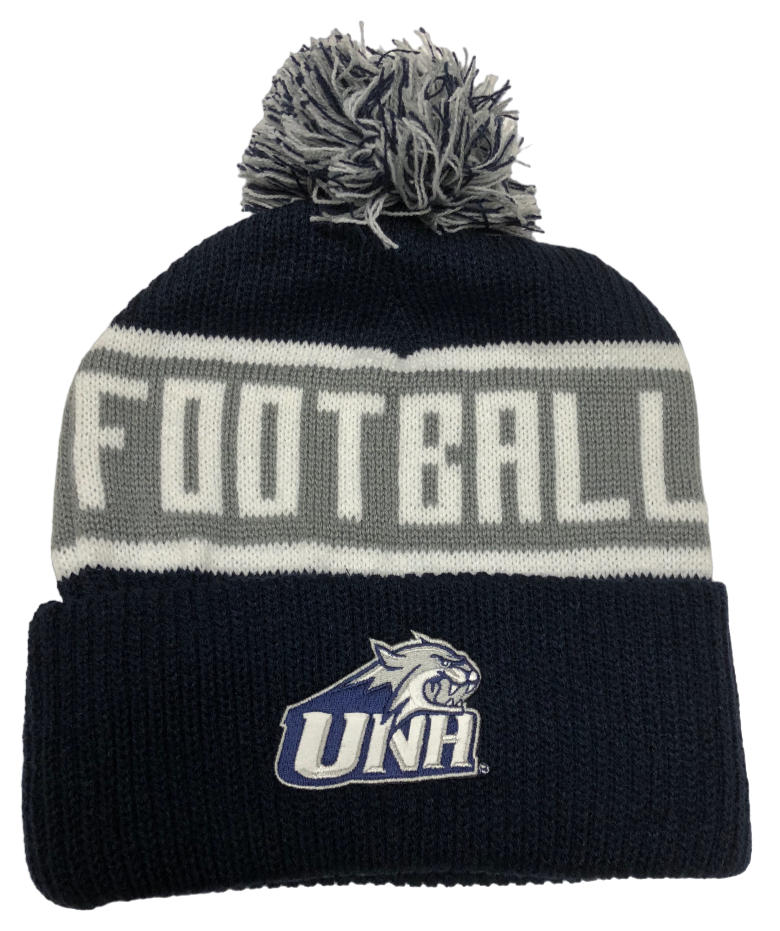 A navy knit winter hat with a white and navy fringe pom on top. The UNH Cathead logo is on the folded brim. The hat has two thin horizontal white stripes bordering a large grey horizontal stripe in the middle of it. Inside the grey stripe, the word "Football" is stitched in white thread in all capital letters.